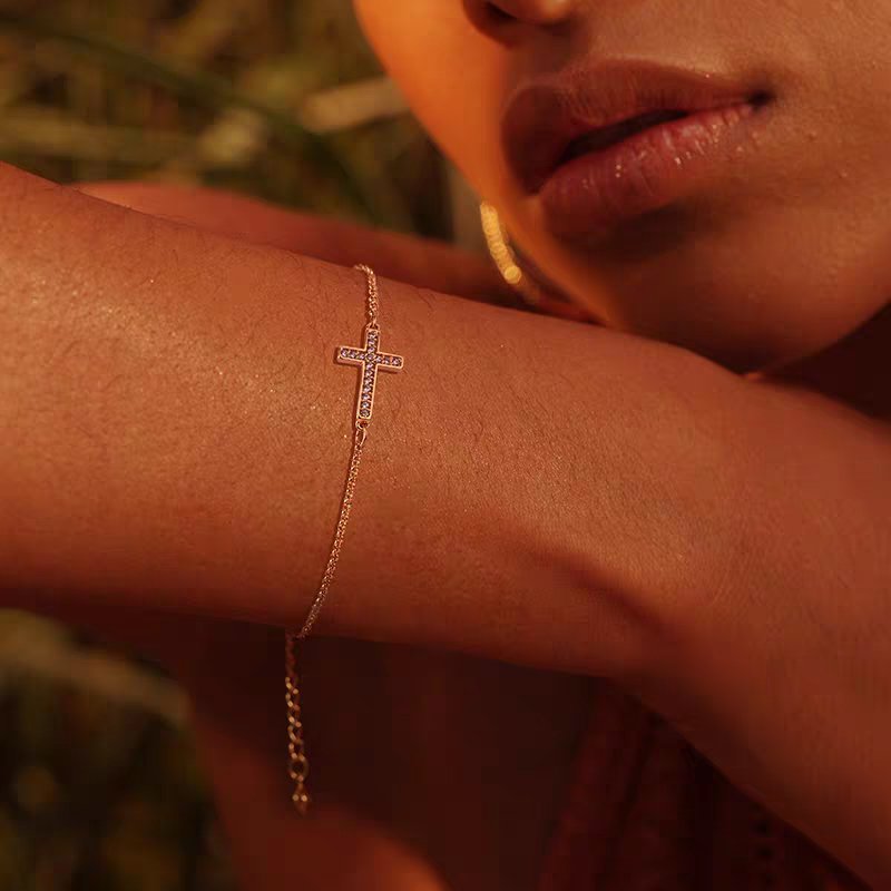 Cubic zirconia cross charm on gold bracelet – close-up view