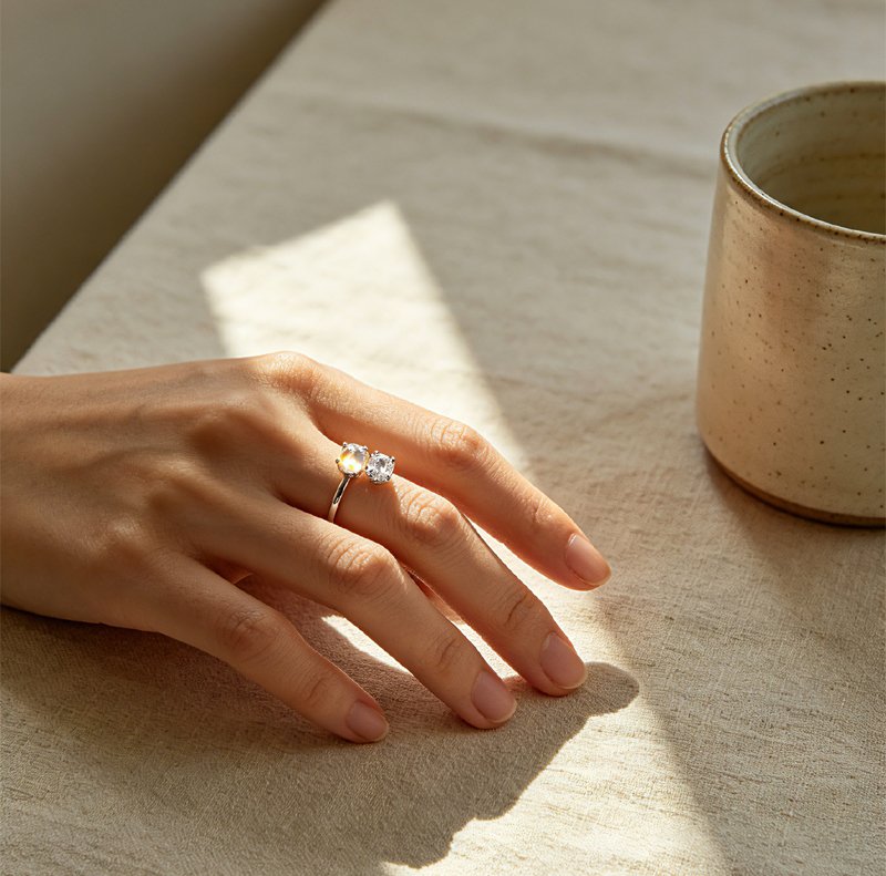 A woman‘s hand wearing a toi et moi ring with two stones side by side on a linen tablecloth
