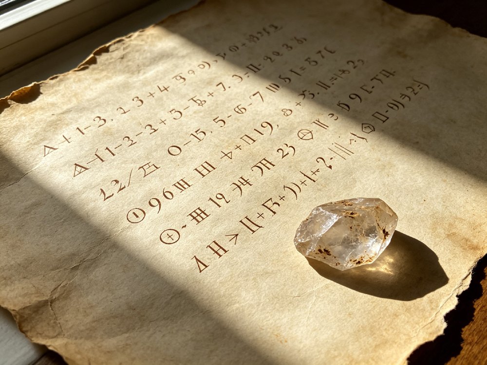 Overhead shot of aged handmade paper with handwritten Pythagorean numerals, a raw uncut crystal cluster resting casually in the corner of the frame, sunlight revealing the paper’s fiber texture.