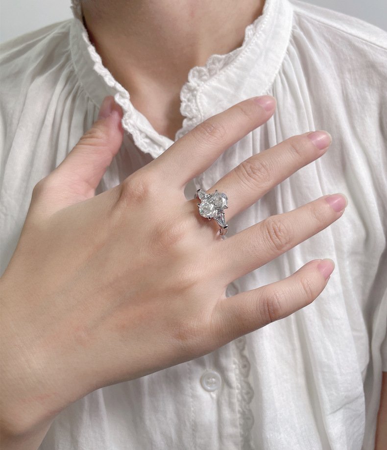 three-stone-oval-moissanite-ring-in-hand Woman wearing an oval moissanite engagement ring, ideal for bridal jewelry.