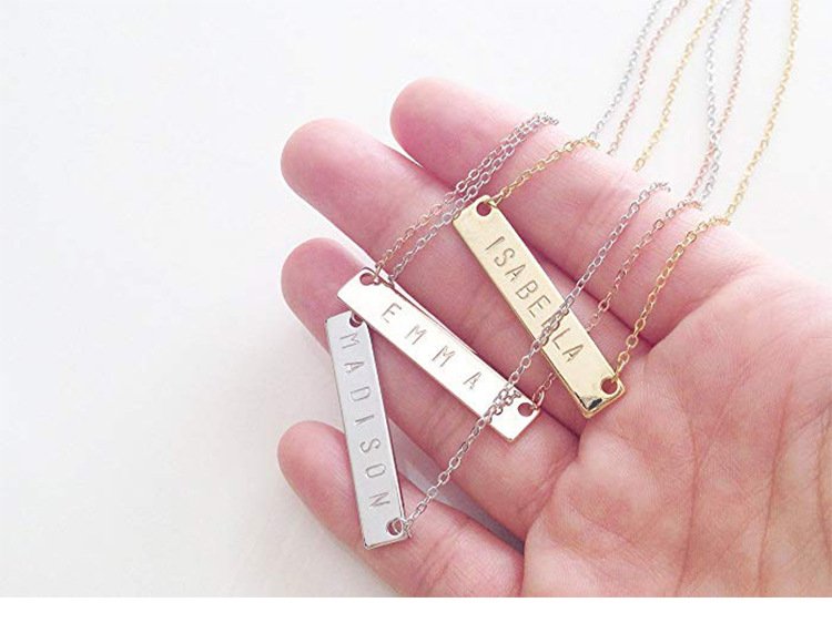 Closeup of hand-engraved bar pendant showing delicate name engraving on polished silver surface.