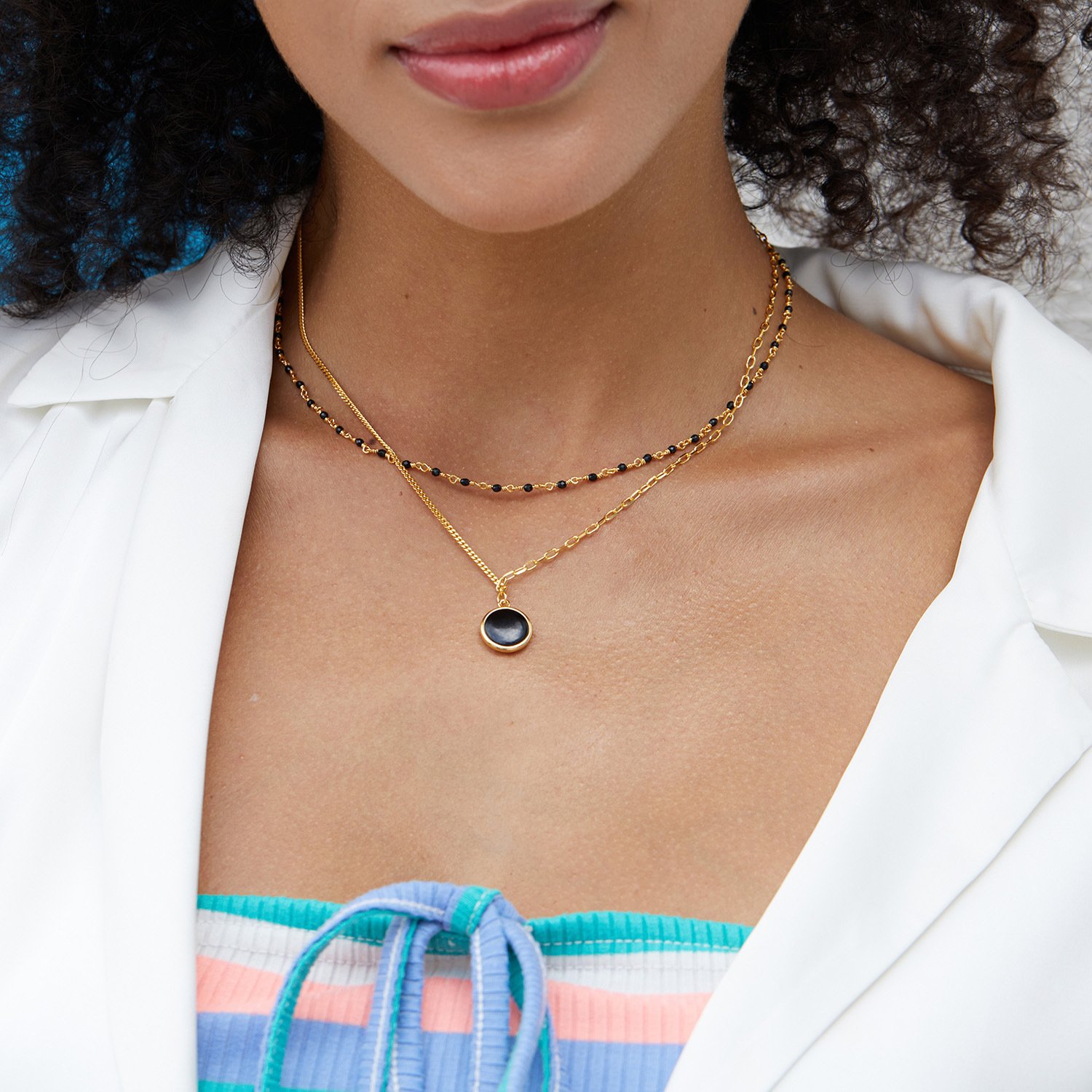 Layered disc necklace on woman paired with thin gold chains. Reversible pendant adds versatility to a stacked jewelry look.